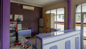 A room with purple walls, a window, a refrigerator, a vending machine, and a small table with flowers. - RedDoorz near RSUD Kebumen (Kebumen)