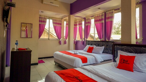 A hotel room with two beds, purple walls, and large windows with pink curtains. - RedDoorz near RSUD Kebumen (Kebumen)