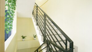 Een trap met een metalen leuning, plantenbakken op de overloop en een muur met een raam aan de linkerkant.