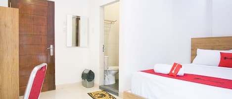A hotel room with a wooden bed, white walls, a red and white bedspread, and a red pillow.