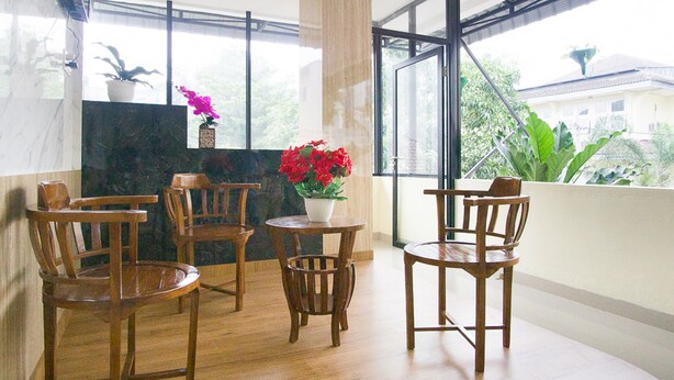 Een balkon met houten stoelen en een tafel, een plant in pot, en uitzicht op groen en gebouwen.