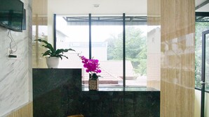 Een modern interieur met een marmeren receptiebalie, een potplant en een houten stoel.