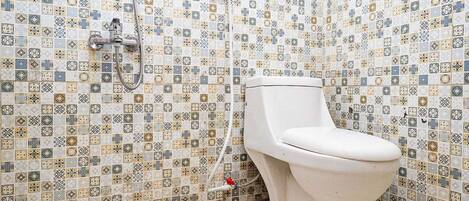 Un baño con pared de azulejos con un motivo geométrico, un inodoro blanco y zona de ducha.