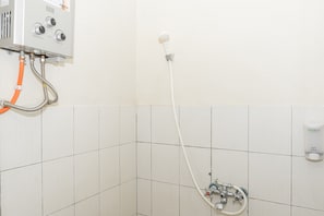 A bathroom with white tiled walls, a shower with a handheld showerhead, and a water heater with control knobs.