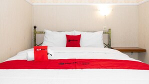 A neatly made bed with white linens and a red blanket, a red pillow, and a small bedside table with a lamp. - RedDoorz near Gajahmungkur Semarang (Semarang)