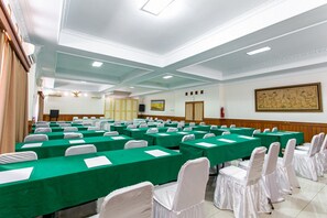 Un salón de conferencias con filas de mesas y sillas, un techo alto con iluminación empotrada y una obra de arte enmarcada en la pared.