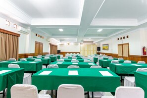 Un salón de conferencias con filas de mesas cubiertas con manteles verdes, sillas blancas y un techo blanco con iluminación empotrada.