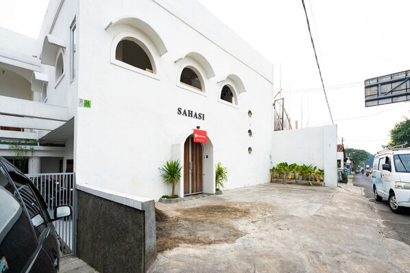 Un bâtiment blanc avec l’inscription « SABASI » sur la façade, une entrée fermée par un portail et un fourgon blanc garé sur le côté droit.