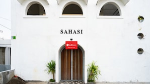 Un edificio con el nombre "SAHASI" sobre una puerta de madera, un letrero de RedDoorz y tres ventanas arqueadas.