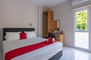Quarto de hotel com cama, secretária de madeira, espelho e janela com vista para árvores.