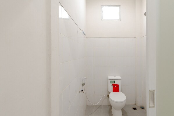 Un baño pequeño y blanco con inodoro, ventana y piso de baldosas.