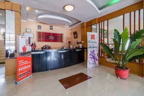 A hotel reception area with a reception desk, a large potted plant, and a banner welcoming guests to the hotel.