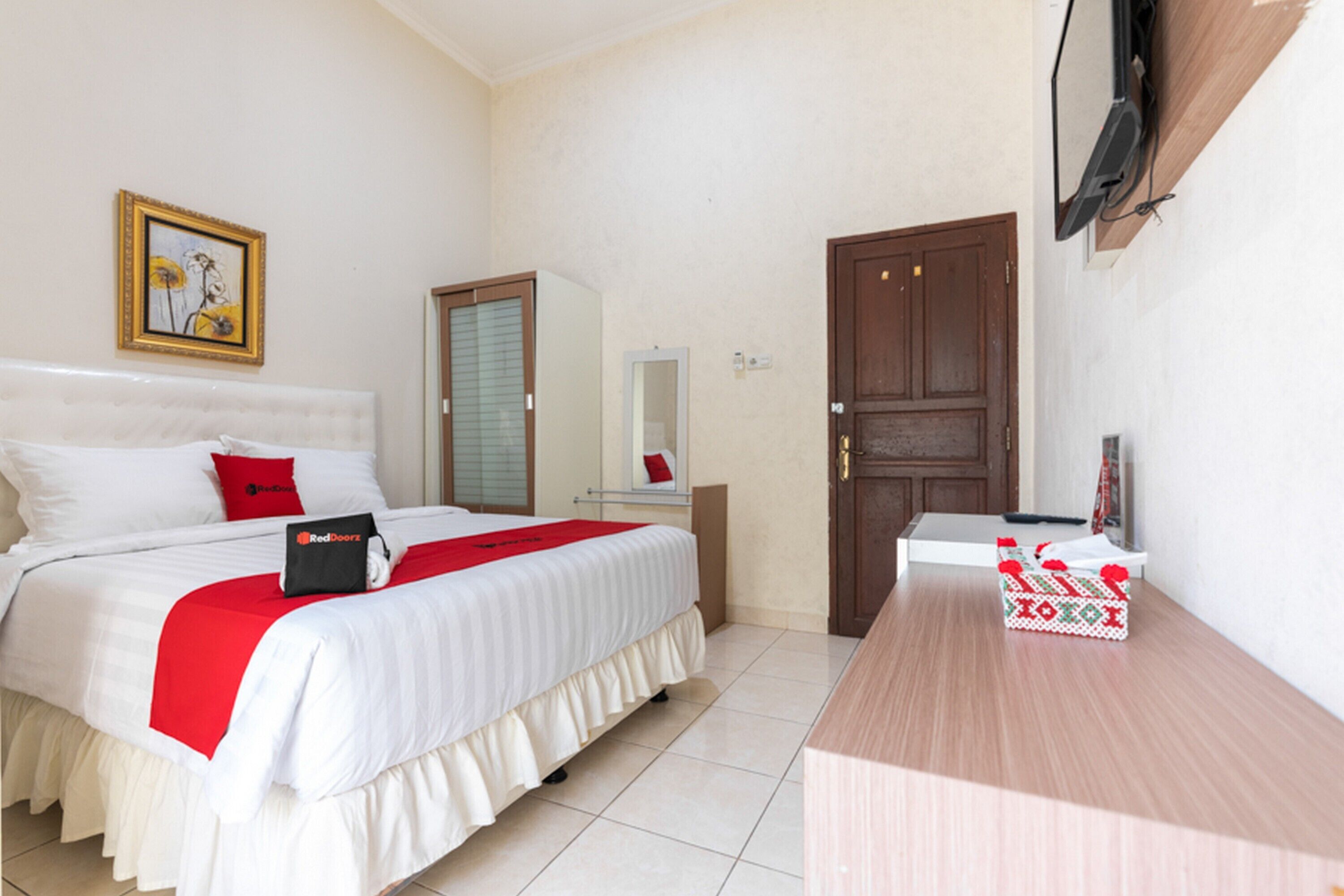 A hotel room with a bed, a desk, a TV mounted on the wall, a door, and a framed picture on the wall.