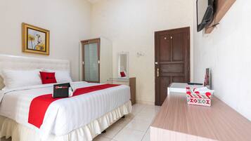 A hotel room with a bed, a desk, a TV mounted on the wall, a door, and a framed picture on the wall.