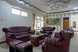 A living room with a dark brown leather sofa set, a coffee table with a floral centerpiece, and a large abstract painting on the wall.