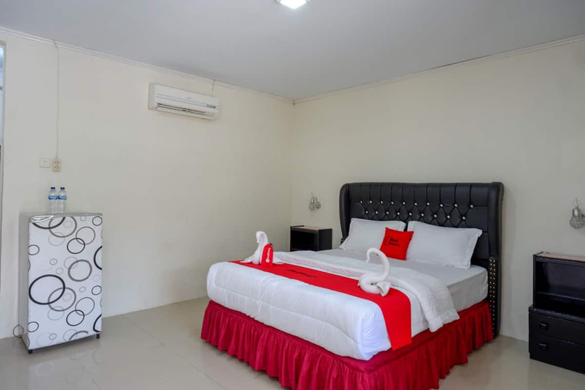 A hotel room with a bed, a desk, and an air conditioning unit.