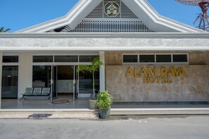The exterior of Alam Raya Hotel with a modern design, featuring a prominent entrance, seating area, and potted plants.