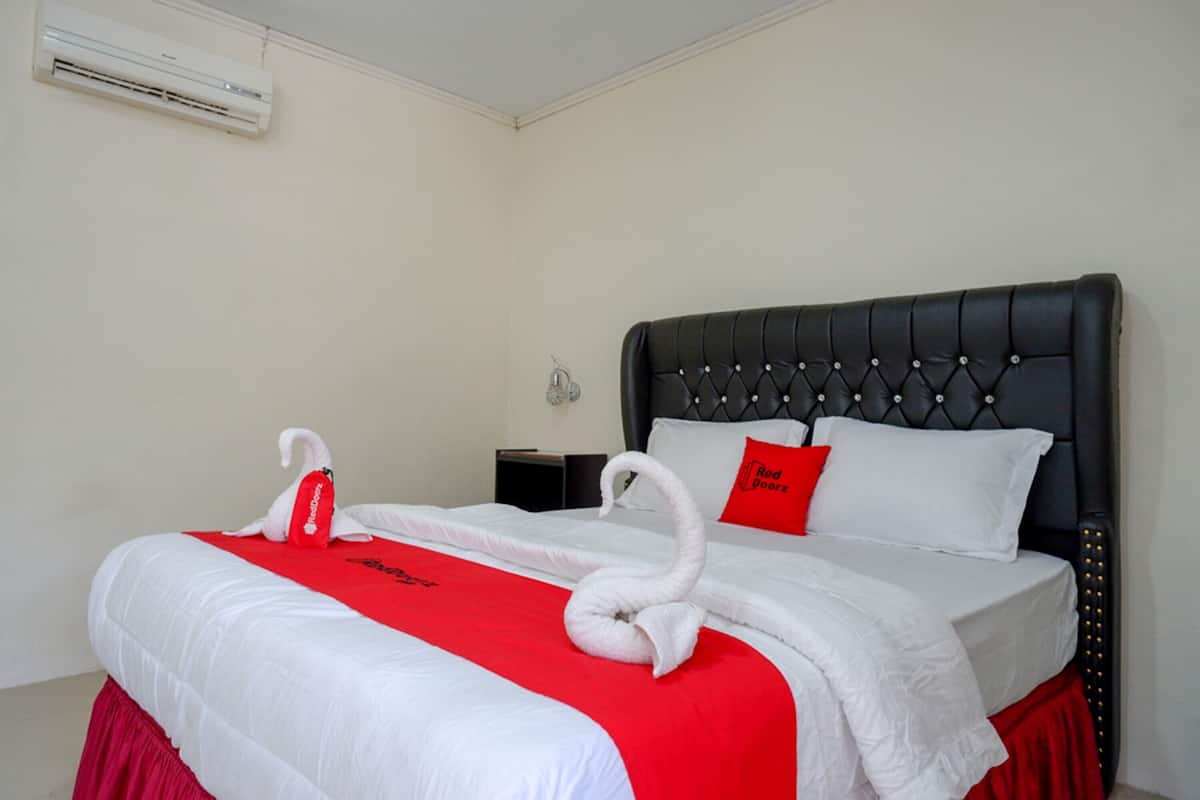 A hotel room with a large bed, a red and white bedspread, a black headboard, and a red pillow.