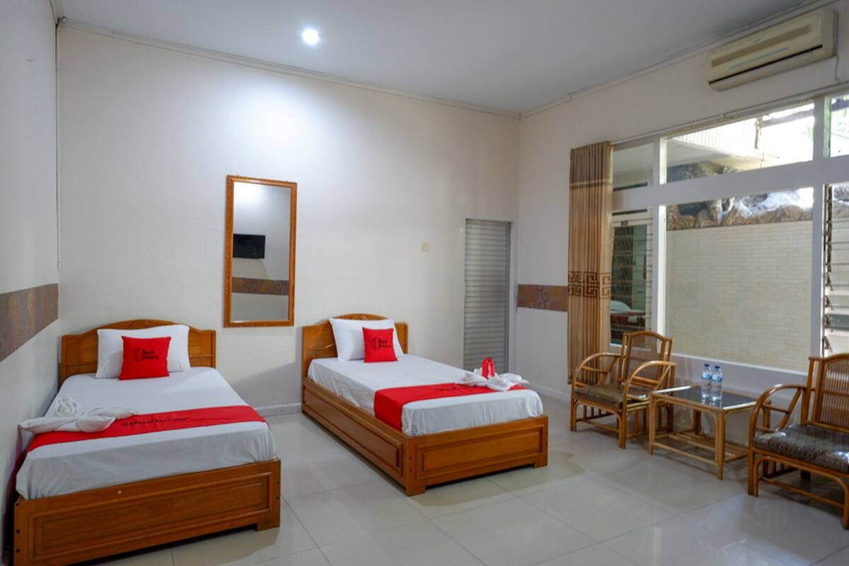 A hotel room with two beds, a small table with chairs, and a large window.