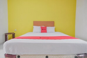 A bed with a wooden headboard, white bedding, and a red accent pillow.