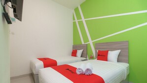Habitación de hotel con dos camas, cada una con cubrecama rojo y blanco, y una pared verde con líneas blancas.
