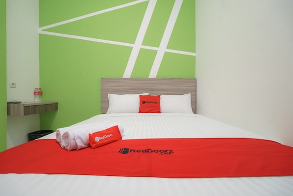 Habitación de hotel con cama, paredes verdes y el logotipo de RedDoorz en las almohadas y la colcha.