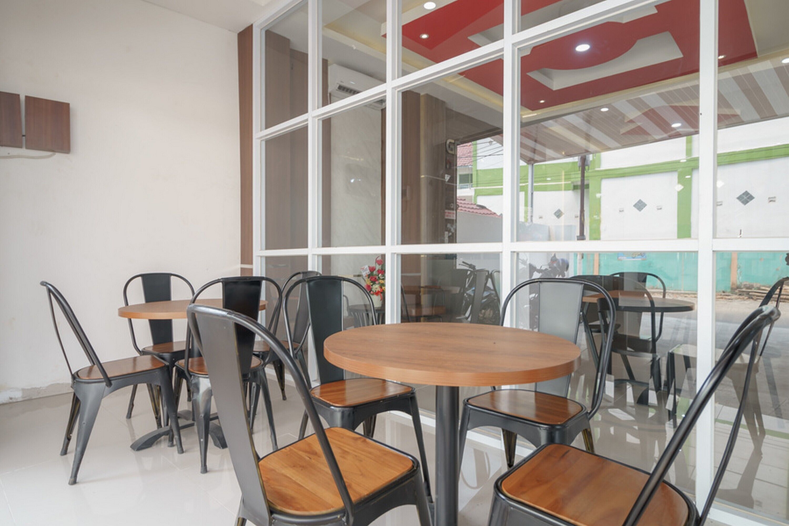 A modern interior with round tables and metal chairs, large windows, and a red ceiling design.