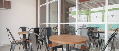 A modern interior with round tables and metal chairs, large windows, and a red ceiling design.