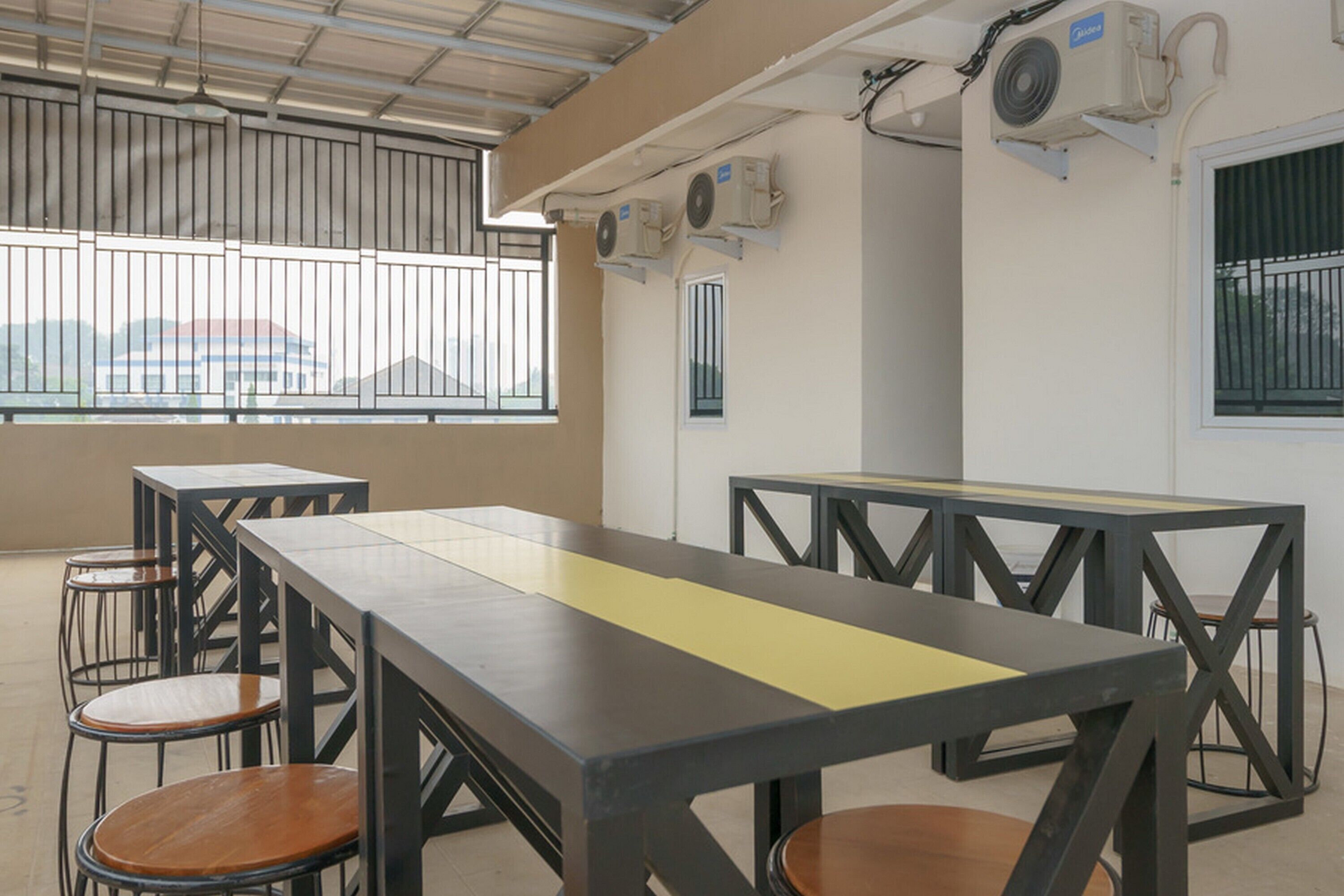 A conference room with a long table and several chairs, air conditioning units on the wall, and a window with bars.