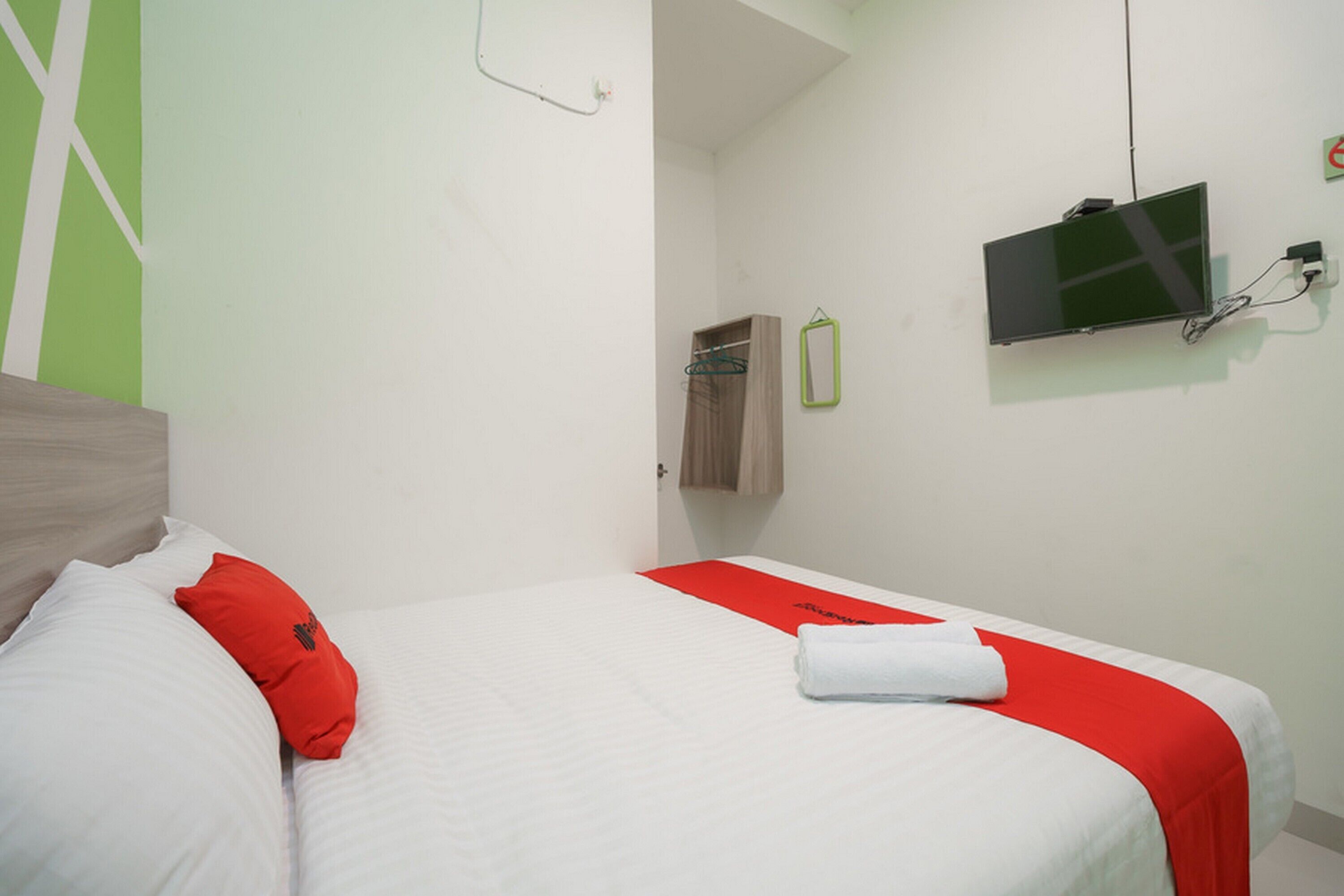 Una habitació d'hotel amb un llit, un televisor fixat a la paret i una tovallola damunt del llit.