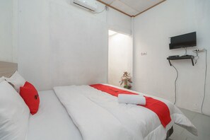 A hotel room with a bed, a TV mounted on the wall, and a small table with a plant.