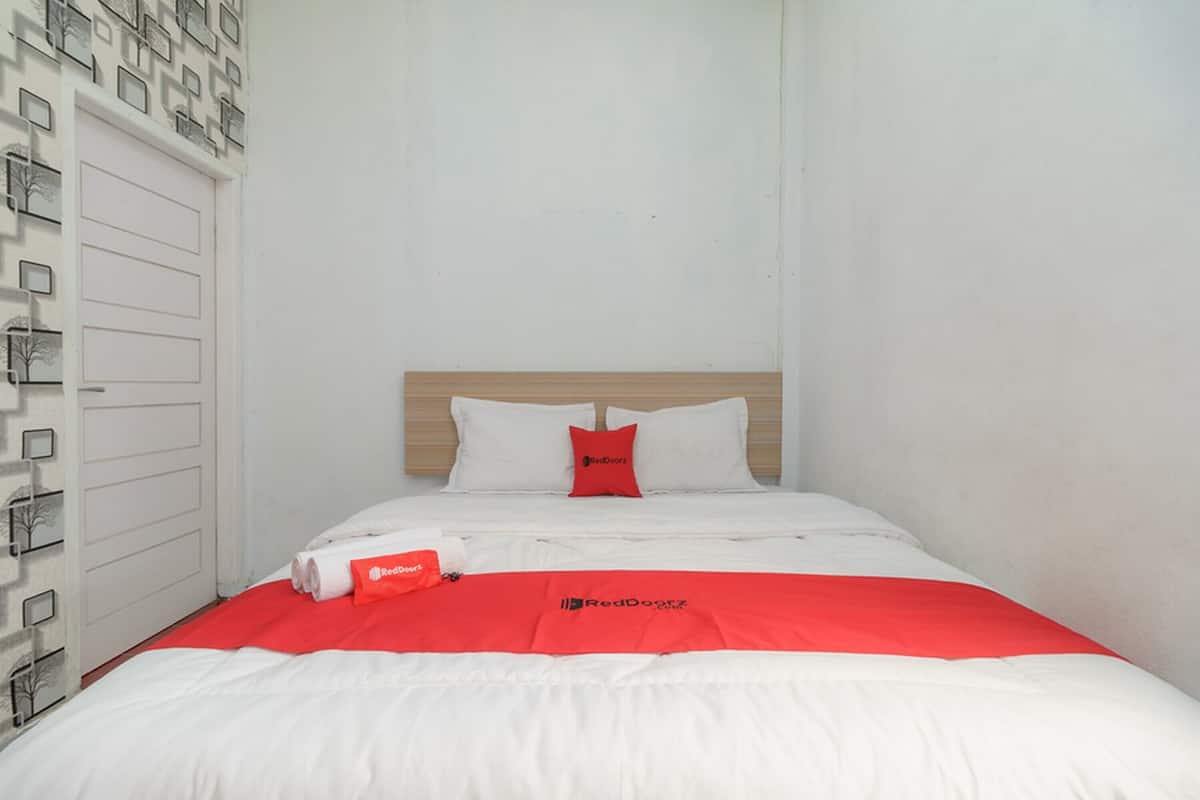 Un lit bien fait, avec une literie blanche et rouge, un oreiller rouge et le logo RedDoor sur la couvre-lit.