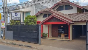 A two-story building with a red and beige facade, a gated entrance, and a sign indicating a business or office. - RedDoorz near IPDN 2 (Cileunyi)