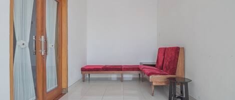 Una habitación pequeña y limpia con una puerta de madera, un banco con cojín rojo, una mesita y una silla.