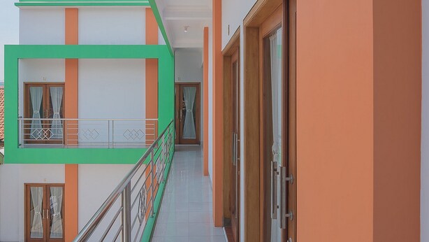 Um edifício de vários andares com fachada verde e laranja, uma varanda com guarda-corpo de metal e uma porta com painel de vidro.