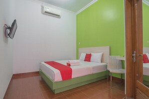 A bedroom with a green wall, a bed with white and red bedding, a chair, and an air conditioning unit. - RedDoorz Plus near Alun Alun Kuningan (Kuningan)