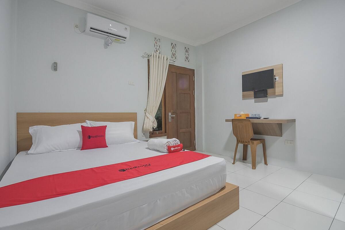 Een hotelkamer met een bed, bureau, stoel, televisie en airconditioning.