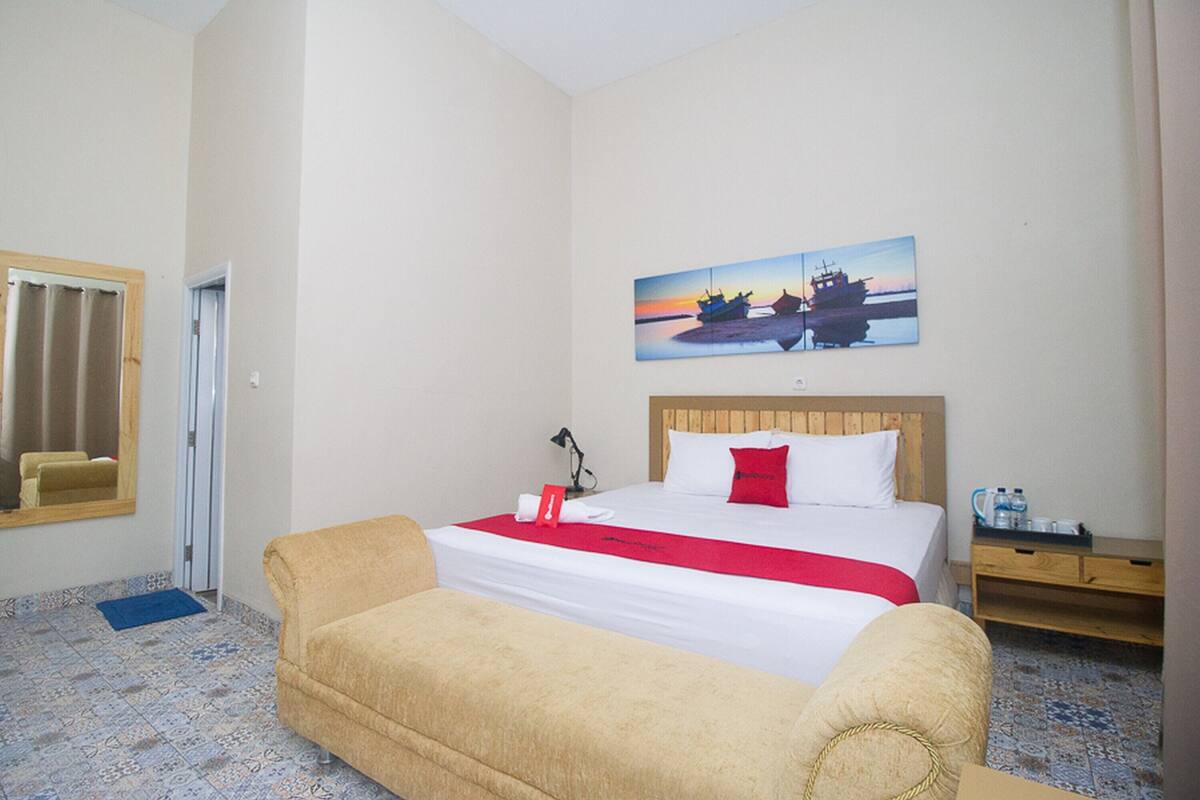 A hotel room with a bed, a sofa, a painting of a boat, and a wooden nightstand.