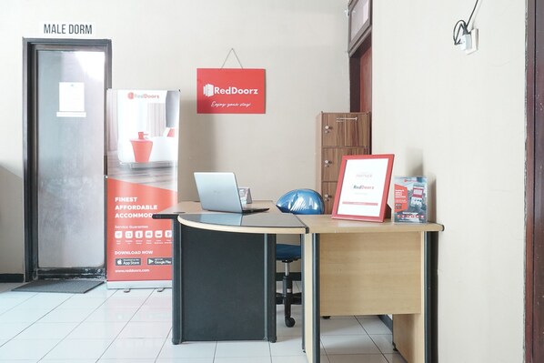 Ein Hotelzimmer mit Schreibtisch, Laptop und einem RedDoorz-Schild. Die Tür ist mit 'MALE DORM' beschriftet.