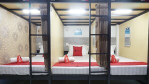 A room with three bunk beds, each with a red blanket and a pillow, and a small table between them. - RedDoorz Hostel @ Borobudur Street (Malang)