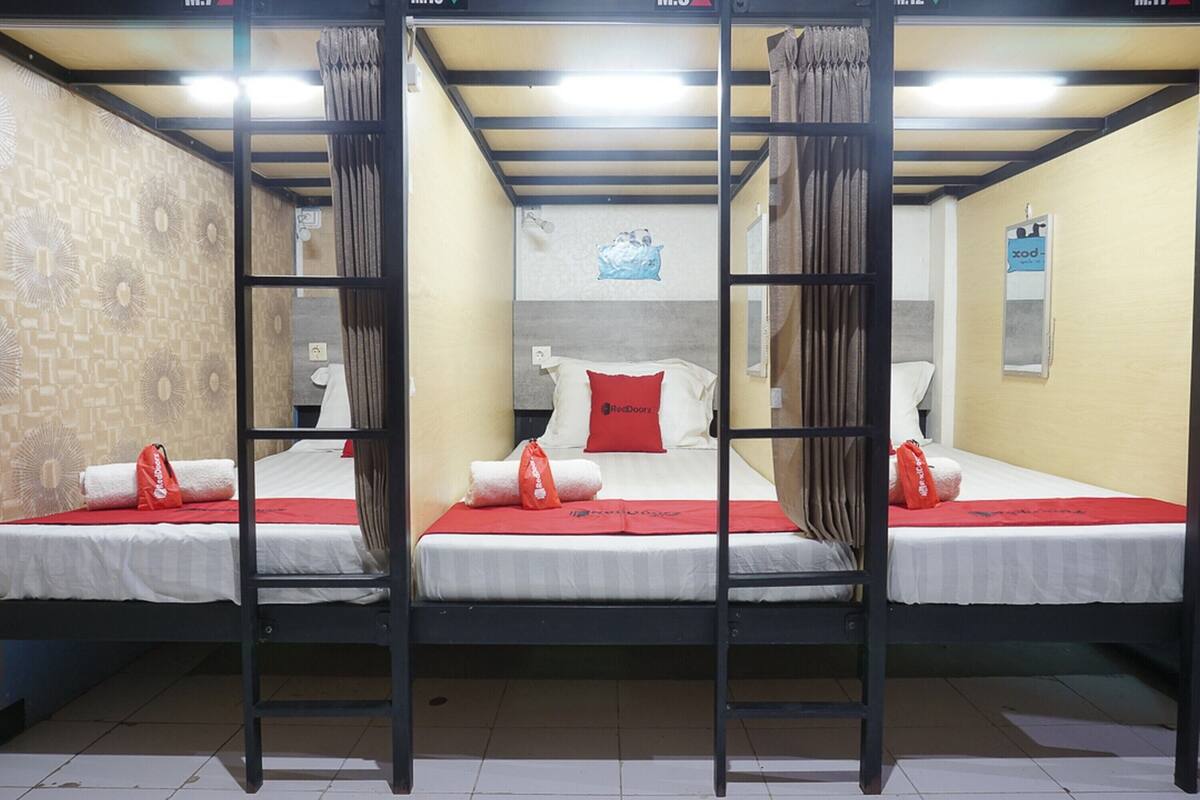 A room with three bunk beds, each with a red blanket and a pillow, and a small table between them.