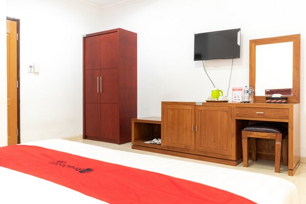 A hotel room with a bed, a wooden wardrobe, a desk with a chair, a television, and a small shelf with items. - RedDoorz Plus Syariah near Java Supermall Semarang 2 (Semarang)