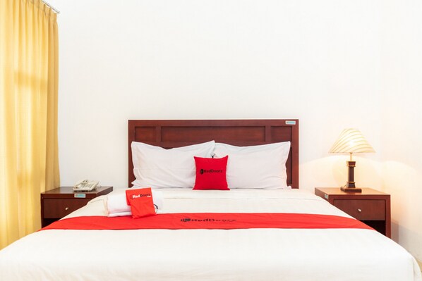 A hotel room with a neatly made bed, a wooden headboard, a nightstand with a lamp, and a telephone. - RedDoorz Plus Syariah near Java Supermall Semarang 2 (Semarang)