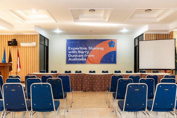 A conference room with a banner reading "Expertise Sharing with Barry Duncan from Australia," blue chairs, a podium, and a projector screen.