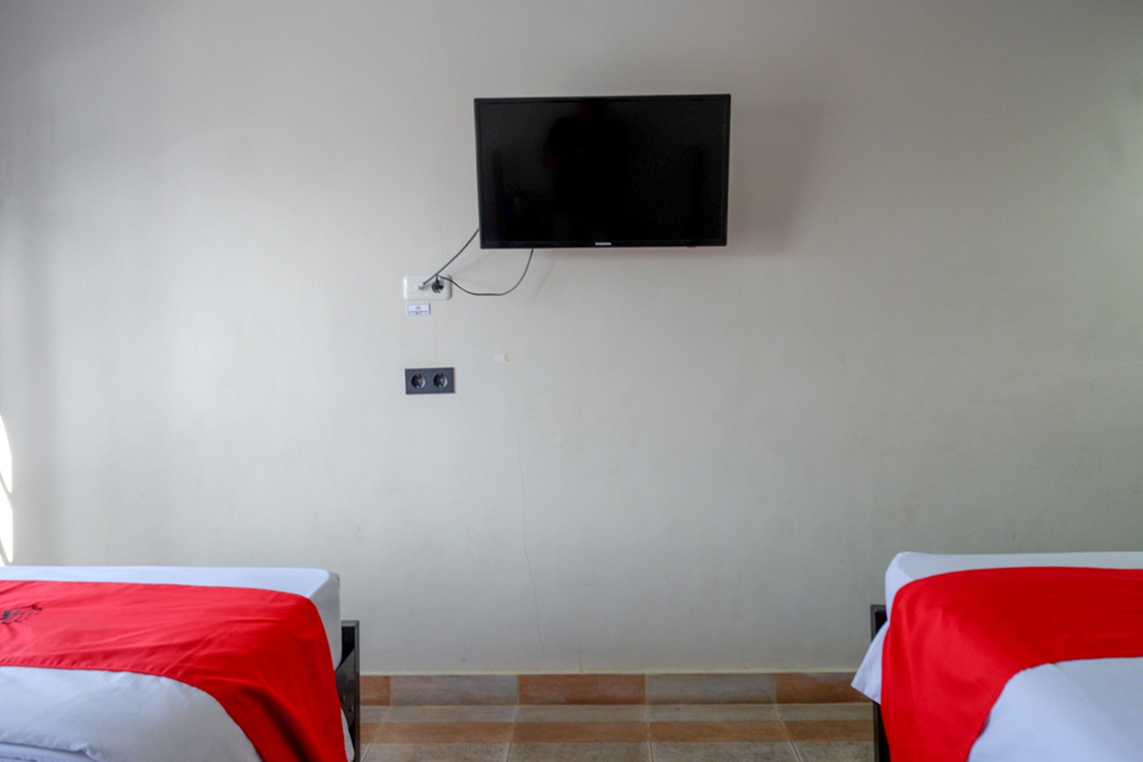 A room with two beds, a television mounted on the wall, and a power outlet.