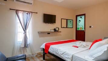 A hotel room with a bed, a chair, an air conditioner, a television, and artwork on the wall.