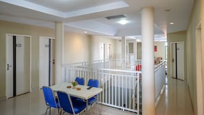 Ein Hotelgang mit Essbereich, inklusive Tisch und Stühlen, weißen Geländern und nummerierten Türen.