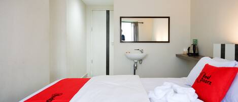 Et hotelværelse med en seng, et hvidt håndvask og et spejl på væggen.