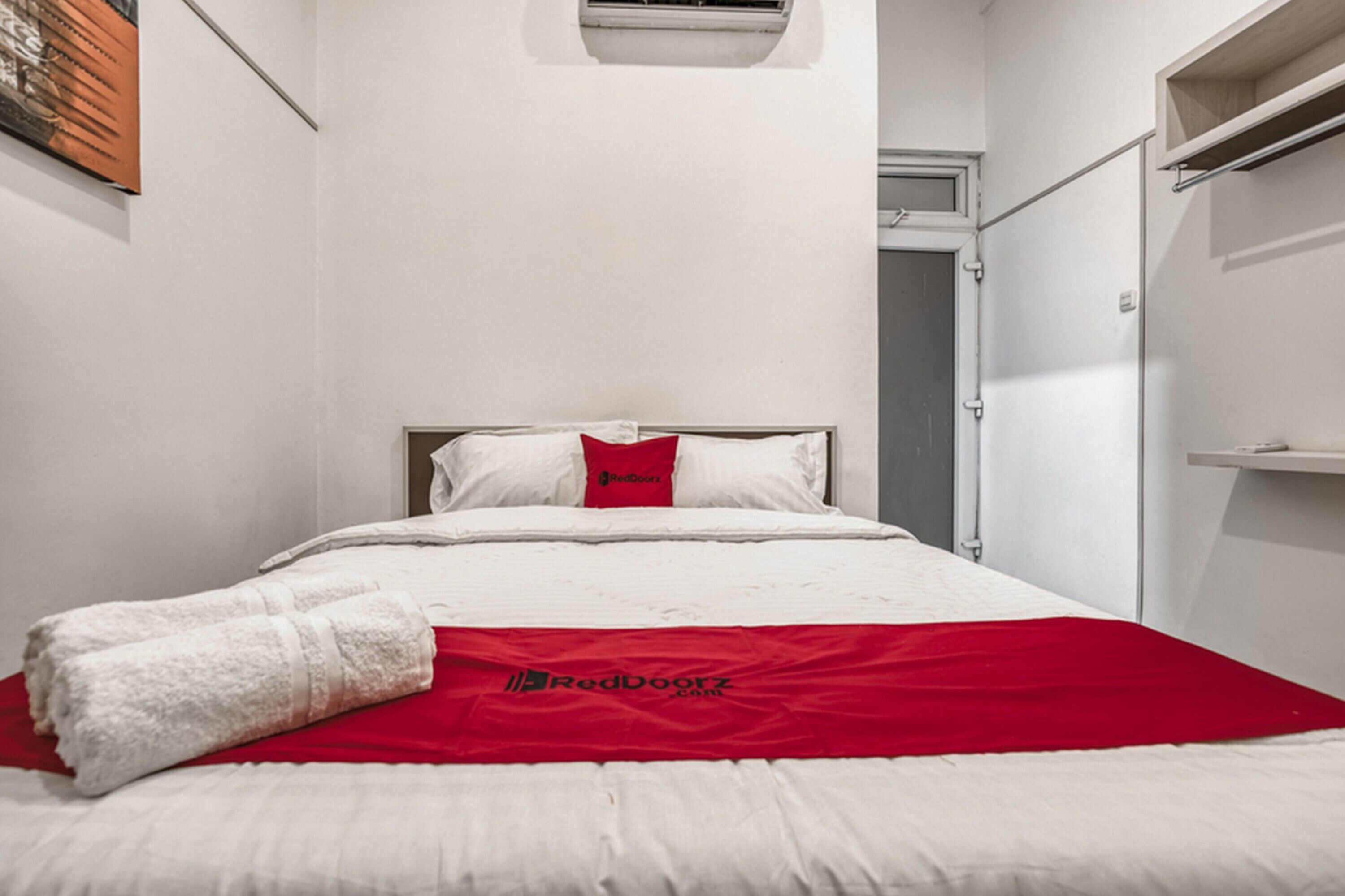 Une chambre d’hôtel avec un lit, une couverture rouge et une serviette blanche.