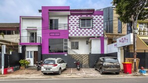 A modern two-story building with a purple and white facade, parked cars, and a visible trash bin. - RedDoorz near Tomang 2 (Jakarta)